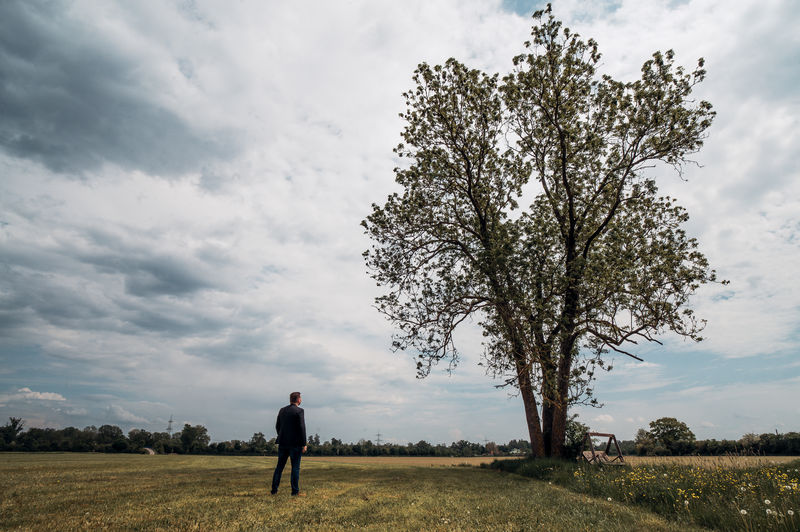 Sad thoughtful but hopeful man in suit stands under a big tree