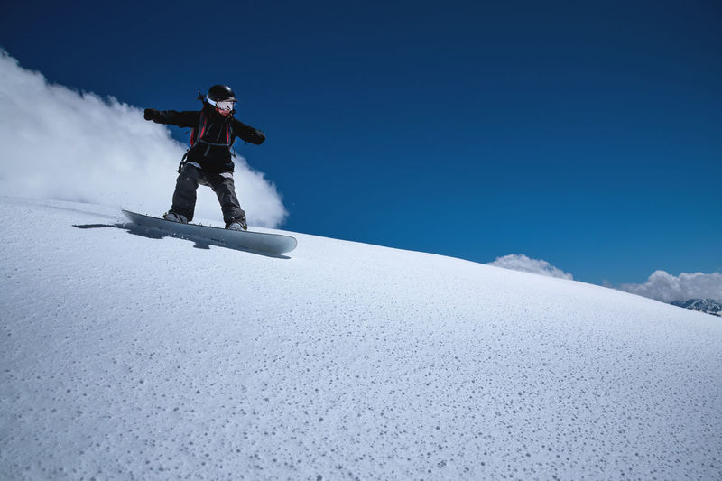 Young sportswoman woman on a snowboard rolls down a snowy slope against a blue sky on a sunny day