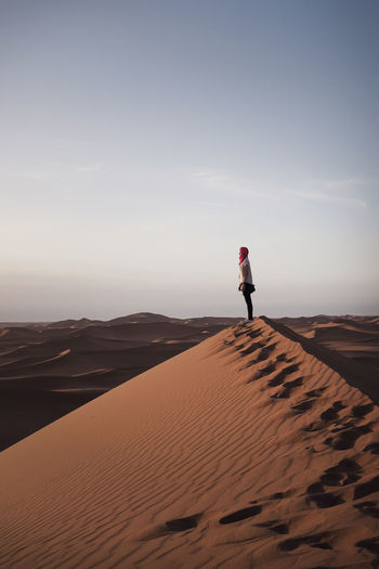 An unknown woman standing on sand dune in desert against sky