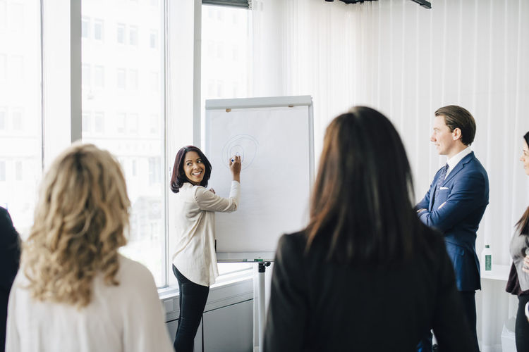 Female entrepreneur talking to colleagues while writing on white board in office seminar