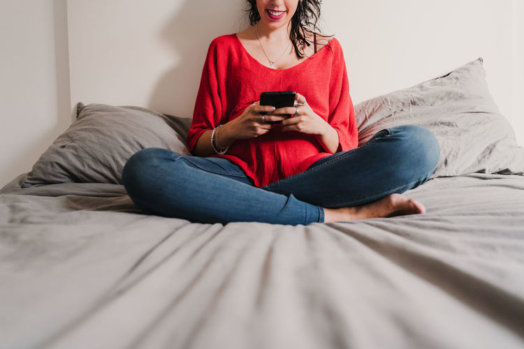 Midsection of woman using phone while sitting on bed at home