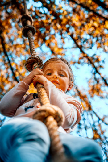 Low angle view of girl swinging against trees