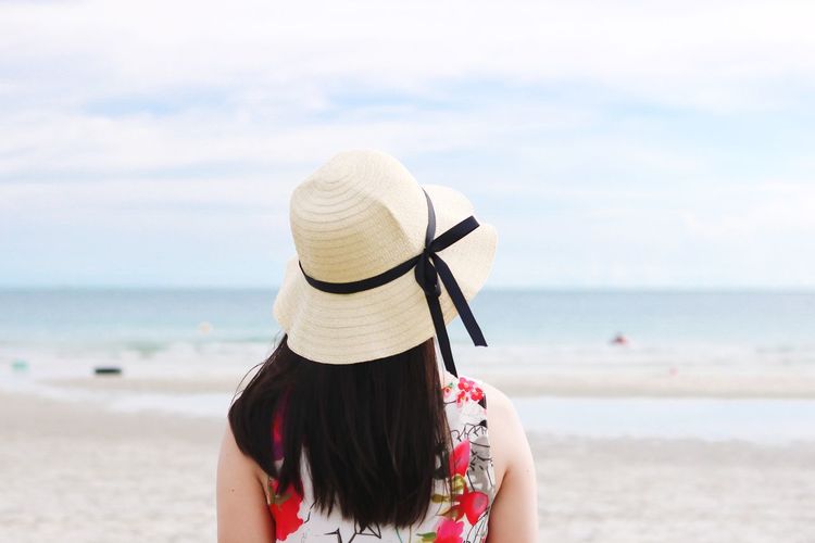 Rear view of woman wearing hat at beach against sky