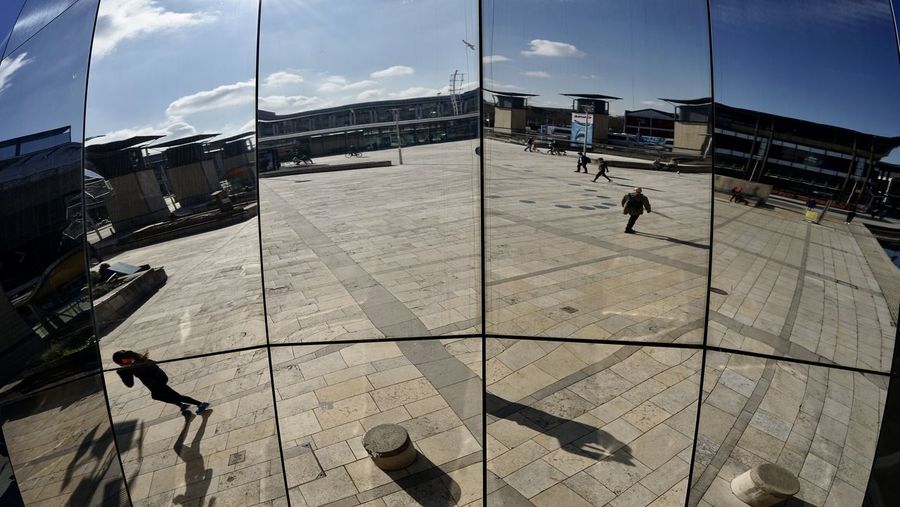 People walking on tiled floor against sky in city