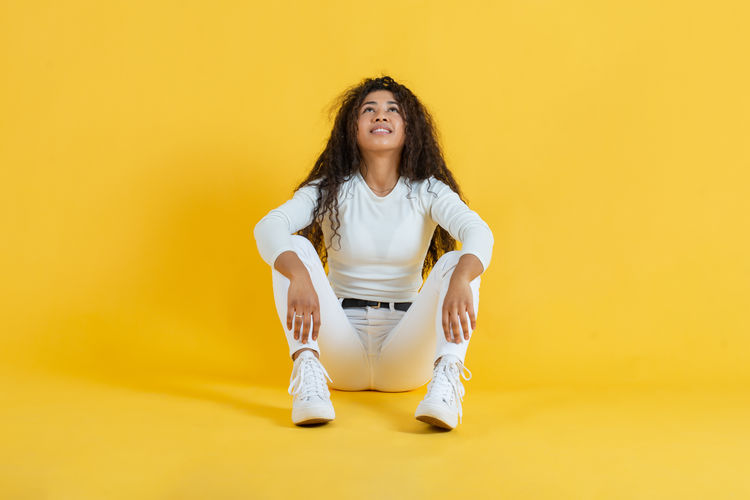 Young woman sitting against yellow background