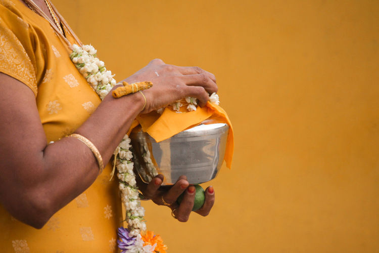 Midsection of woman holding religious utensil against yellow