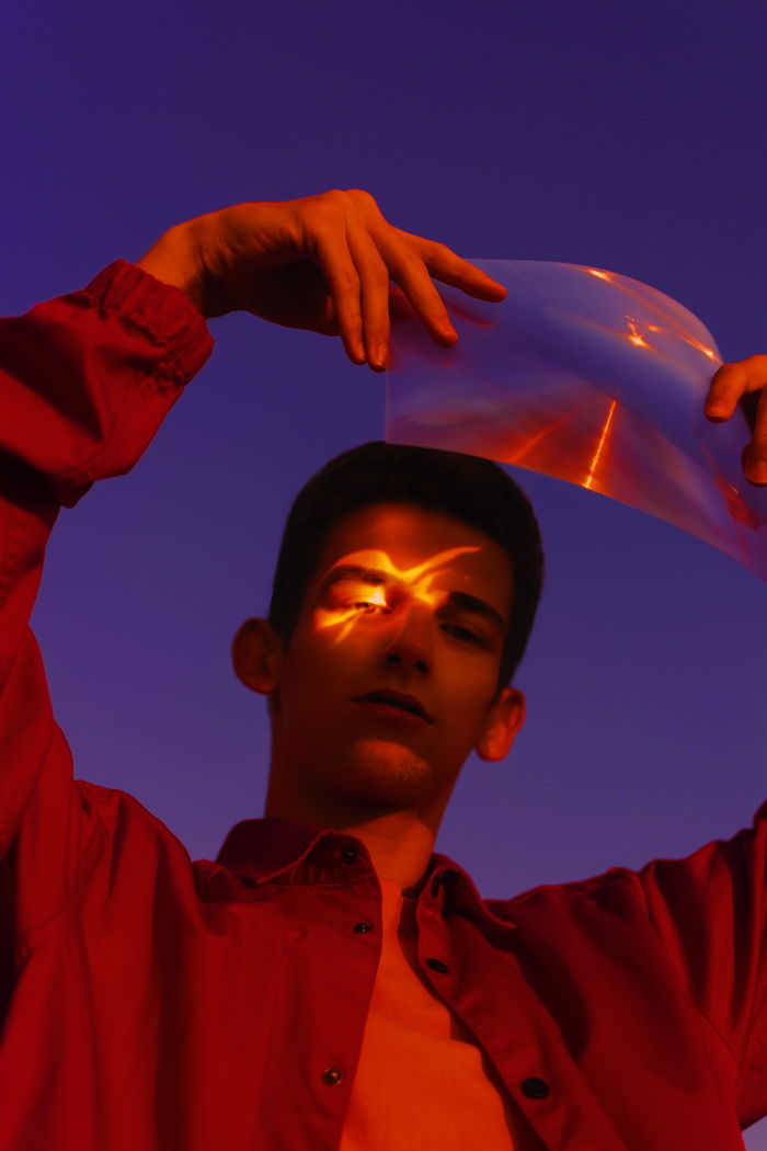 Low angle portrait of man holding plastic against sky at night