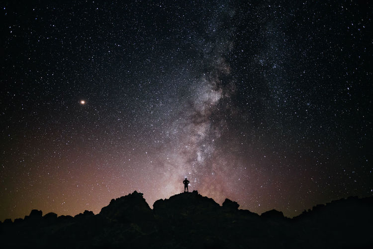 Silhouette man standing on mountain against star field at night
