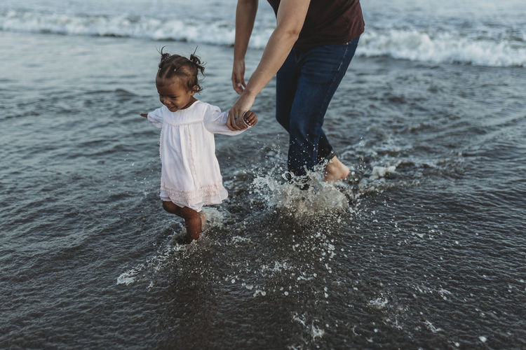 Young toddler girl splashing in the sea with family