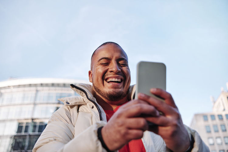 Portrait of smiling man using smart phone against sky
