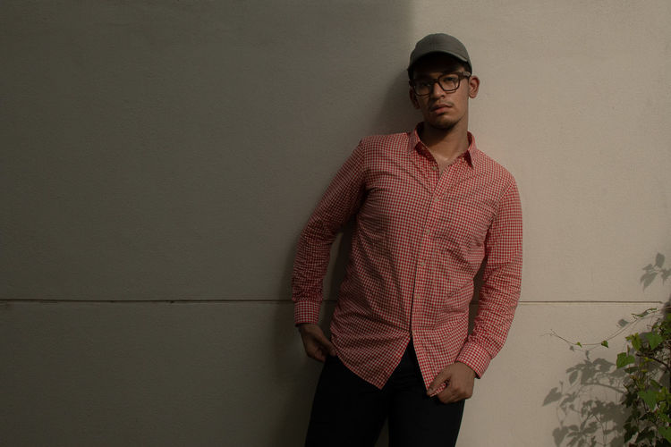 Young man with red checkered shirt and grey leather cap standing against wall
