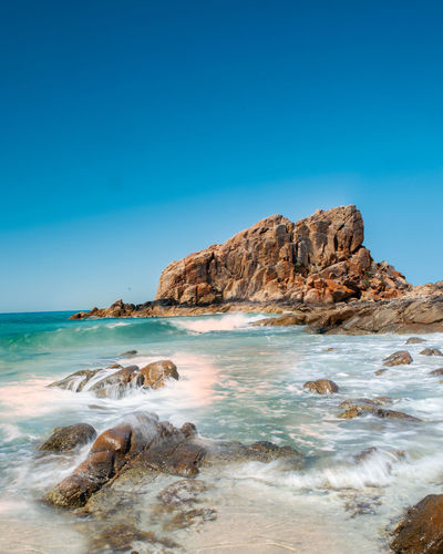 Rocks on beach against clear blue sky