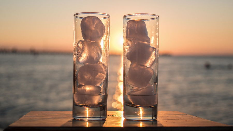 Close-up of beer glass on table against sea during sunset