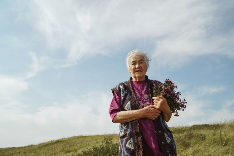 Amature woman holding bouquet of flowers standing on field against sky