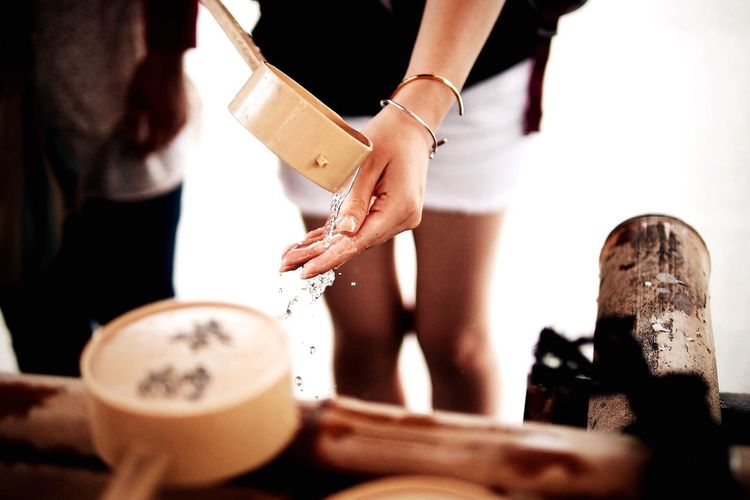 Midsection of woman pouring water on hand through wooden ladle