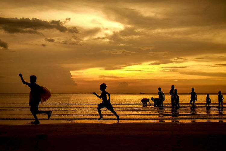 Silhouette people playing on beach against sky during sunset
