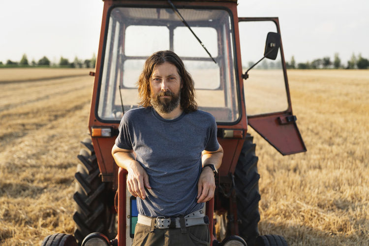 Mature man leaning on tractor at farm