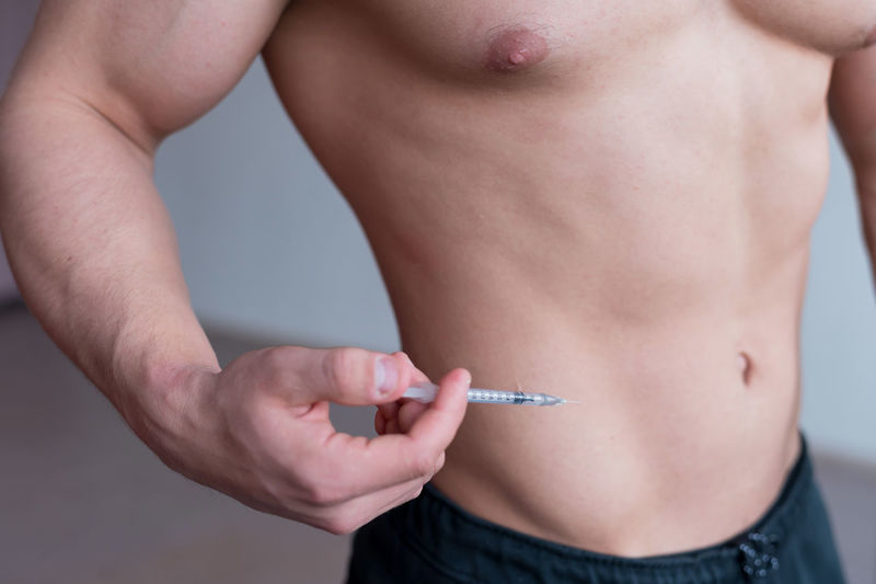 Midsection of shirtless man holding syringe