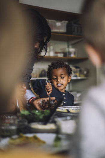 Female teacher serving food to boy while having breakfast in kindergarten