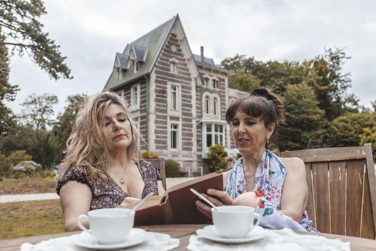 Couple of mature friendly women on vacation drinking tea and reading a book outdoors