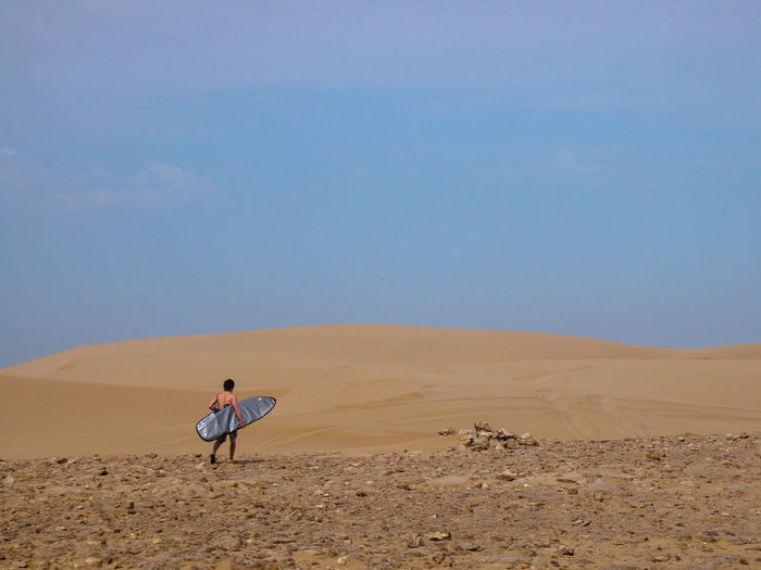 A surfer walking through the desert to find another secret spot